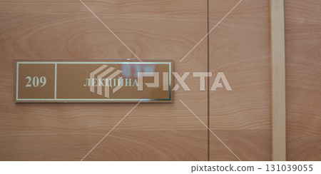 Door sign, doorplate hangs on light gray wooden. 131039055