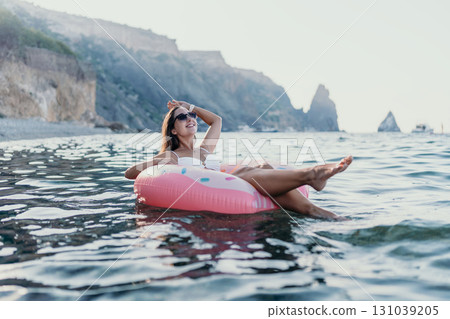 Woman, ocean, relaxation. Happy woman floats on donut in calm sea with coastal cliffs. Woman, ocean, relaxation. Happy woman floats on donut in calm sea with coastal cliffs. 131039205