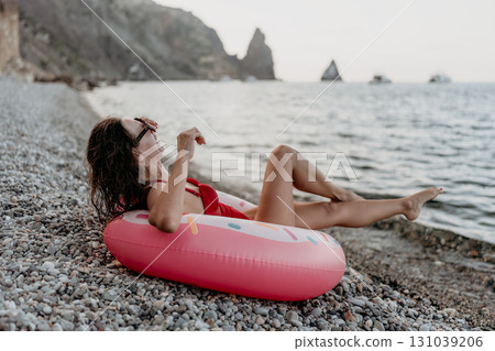 Woman, beach, vacation. Relaxing woman on a pebble beach with donut float enjoying sea and cliffs view. Woman, beach, vacation. Relaxing woman on a pebble beach with donut float enjoying sea and cliffs view. 131039206