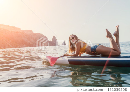Woman Paddleboarding Ocean Coastline - Relaxing on a paddleboard on the ocean with rocky cliffs in the background. 131039208
