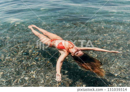 Woman Floating Sea Red Bikini - A woman in a red bikini floats on her back in the clear water of a sea. Woman Floating Sea Red Bikini - A woman in a red bikini floats on her back in the clear water of a sea. 131039314