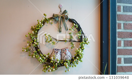Charming rustic wreath with cute fabric owls and green berries on a light wall, cozy home decor Charming rustic wreath with cute fabric owls and green berries on a light wall, cozy home decor 131039648