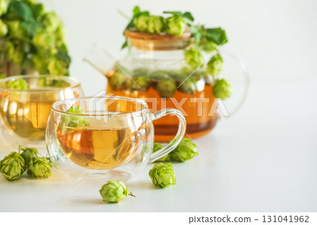 Hop Tea in Glass Teapot and Cups with Fresh Hops on Table 131041962