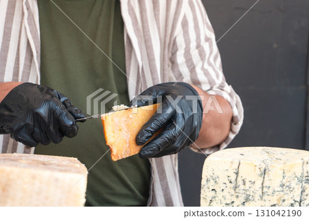 A vendor slices a piece of cheese with a knife at a farmers market A vendor slices a piece of cheese with a knife at a farmers market 131042190