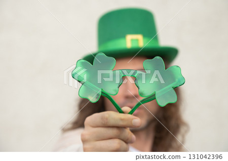 Happy Man with funny Shamrock clover glasses and Green St. Patrick's Hat against beige wall. Close up. 131042396