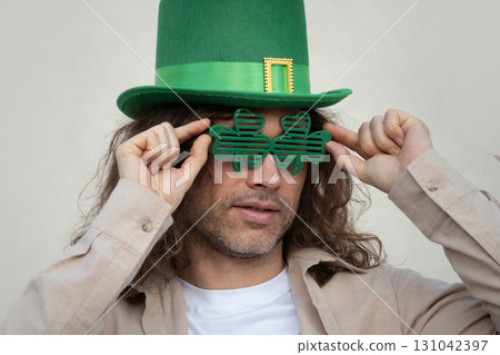 Bearded caucasian Man Wearing Shamrock clover glasses and Green St. Patrick's Hat against beige wall. Space for design. 131042397