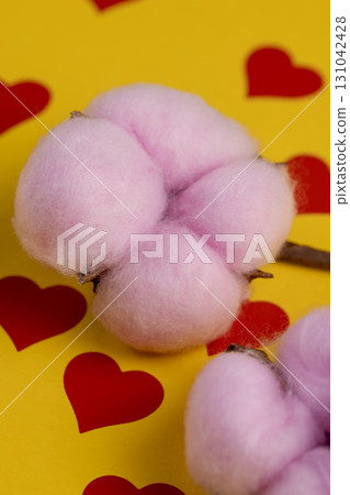 cotton flowers with pink-colored cotton wool lie on yellow paper with red hearts, several twigs of hand-made cotton flowers and a heart symbol on the yellow surface 131042428