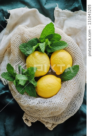 Fresh Lemons and Mint Leaves Arranged in a Natural Basket on a Dark Fabric Surface 131043205