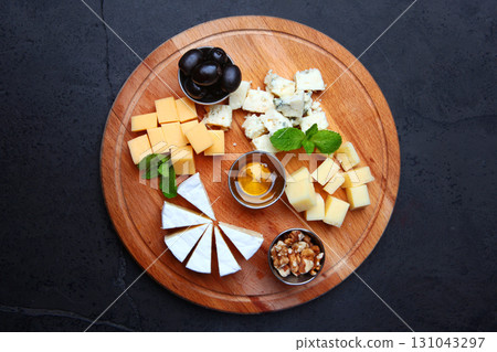 Assorted cheeses on wooden tray. View from above. Dark background. Honey, olives and walnuts on a plate. Copy space. Assorted cheeses on wooden tray. View from above. Dark background. Honey, olives and walnuts on a plate. Copy space. 131043297