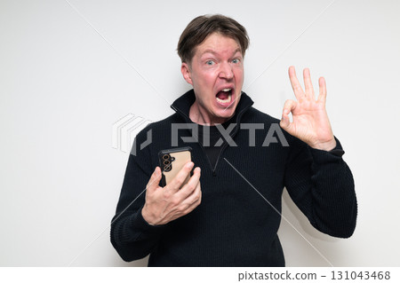 Scandinavian mid adult man using phone against white background making OK sign gesture Scandinavian mid adult man using phone against white background making OK sign gesture 131043468