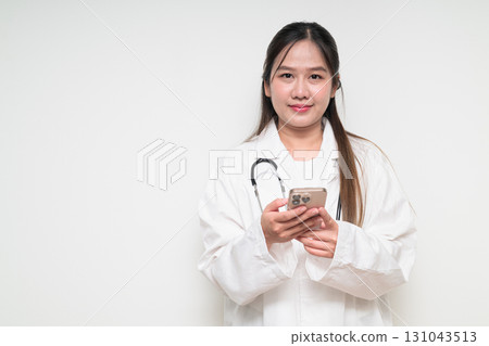 Portrait of Southeast Asian healthcare worker woman doctor in lab coat using mobile phone 131043513