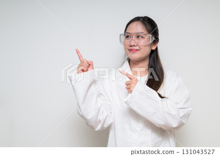 Asian healthcare worker scientist woman in lab coat with safety goggle glasses pointing finger up 131043527