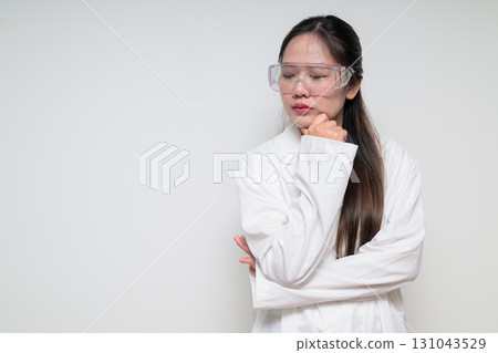 Asian healthcare worker scientist woman in lab coat wearing safety goggle glasses thinking 131043529