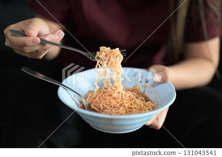 Close-up of Asian woman sitting at home in sofa eating instant noodles from bowl Close-up of Asian woman sitting at home in sofa eating instant noodles from bowl 131043541