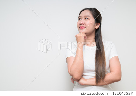 Portrait of young Asian woman with hand on chin planning and looking up against white background 131043557