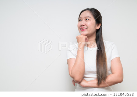 Portrait of young Asian woman with hand on chin planning and looking up against white background Portrait of young Asian woman with hand on chin planning and looking up against white background 131043558