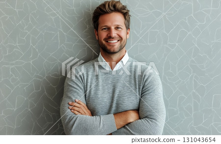 Smiling Man Stands Confidently Against a Textured Gray Wall at an Indoor Setting 131043654