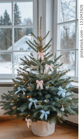 A beautifully decorated Christmas tree with pastel pink bows stands in a bright room with winter views A beautifully decorated Christmas tree with pastel pink bows stands in a bright room with winter views 131043926