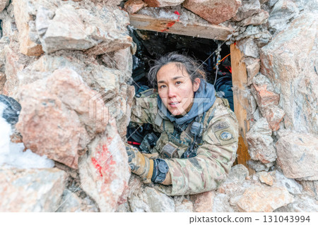 Asian woman in military gear emerging from rocky shelter in a rugged mountainous environment 131043994