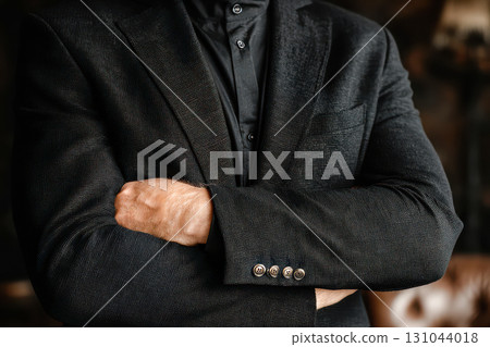 Confident man in black suit with crossed arms, exuding professionalism and authority in a stylish setting 131044018