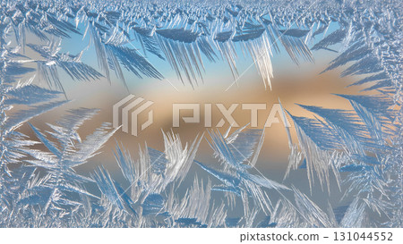 A close-up of beautiful ice patterns forming a frame on a windowpane. The ice crystals create unique and intricate designs reminiscent of ferns or feathers. A blurred, light background is visible thro 131044552