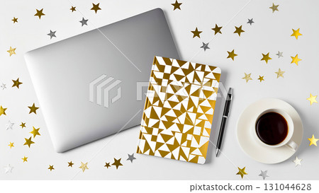 An overhead view of a workspace decorated in a festive theme. A closed laptop, a gold notebook with a geometric pattern, a black pen, and a cup of coffee lie against a white background. Scattered arou 131044628