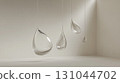 Translucent teardrop glass sculptures suspended from white ceiling, creating ethereal light play within minimalist interior space with pristine walls and flooring 131044702