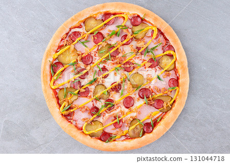 Cheeseburger Style Pizza with Pickles, Sausage, Ham, Mustard Drizzle, Fried Onions, and Green Onions on Golden Crust over Gray Stone Background 131044718