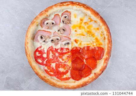 Four-Flavor Pizza with Cheese, Pepperoni, Ham and Mushroom, and Tomato Sections on Baked Crust over Gray Stone Background 131044744