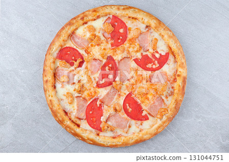 Pizza with Ham, Chicken, Fresh Tomato Slices, and Melted Cheese on Golden Crust over Gray Stone Background 131044751
