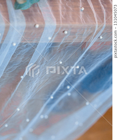 Close-up of a sheer fabric panel adorned with elegant pearl embellishments. The soft texture and intricate detailing create a delicate, captivating visual element, perfect for design inspiration 131045073