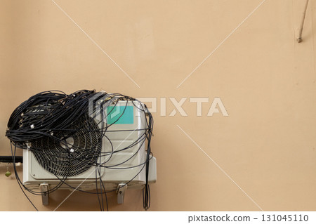 An air conditioner with large coil of wires for connection is installed on facade of the house. An air conditioner with large coil of wires for connection is installed on facade of the house. 131045110