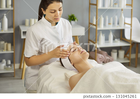 Professional female performing facial massage to young woman  131045261