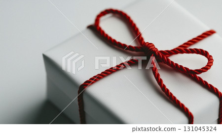 Elegant white gift box adorned with a vibrant red twisted rope bow Elegant white gift box adorned with a vibrant red twisted rope bow 131045324