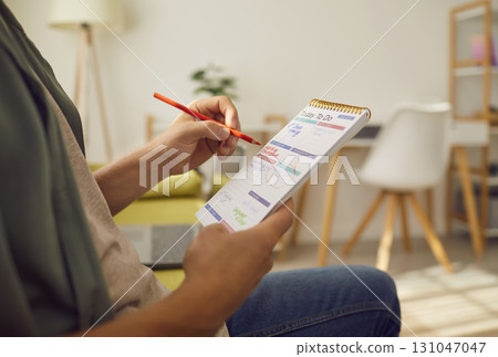 Man sitting on sofa at home planning tasks and to do list in his notepad. 131047047