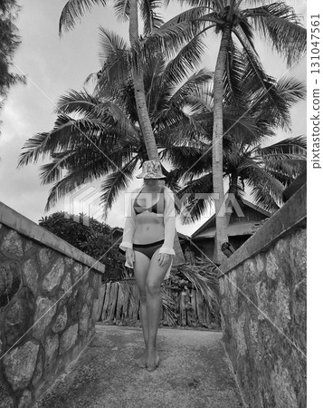 A woman walks barefoot down a tropical path lined with palm trees. A woman walks barefoot down a tropical path lined with palm trees. 131047561