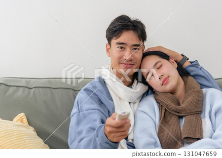 Winter finds happy couple relaxing comfortably at home, enjoying quiet day together. Man holds television remote control, woman rests head peacefully on his shoulder, embracing warmth winter cold. Winter finds happy couple relaxing comfortably at home, enjoying quiet day together. Man holds television remote control, woman rests head peacefully on his shoulder, embracing warmth winter cold. 131047659