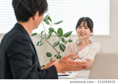 A mother holding a baby receiving advice from a salesman during a door-to-door sales call, a female customer A mother holding a baby receiving advice from a salesman during a door-to-door sales call, a female customer 131048919