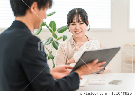 A mother holding a baby receiving advice from a salesman during a door-to-door sales call, a female customer A mother holding a baby receiving advice from a salesman during a door-to-door sales call, a female customer 131048920