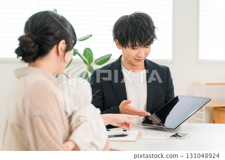 一名男銷售員正在用平板電腦向一名抱著嬰兒的女顧客講解 一名男銷售員正在用平板電腦向一名抱著嬰兒的女顧客講解 131048924