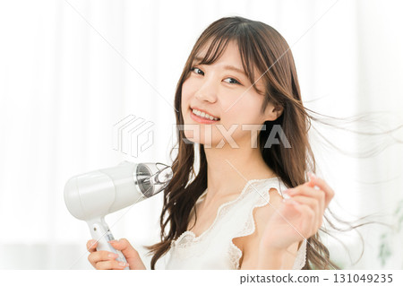 A woman blow-drying her hair with a hair dryer (hair care) 131049235