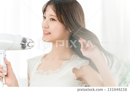 A woman blow-drying her hair with a hair dryer (hair care) 131049238