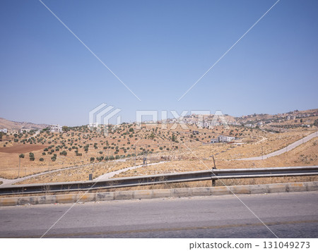[Jordan] A clear sky and a desert landscape covered with olive trees seen from the window of a car traveling on a road on the outskirts of the capital Amman 131049273