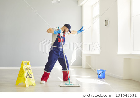 Professional cleaner from cleaning service having fun, dancing with mop while washing floor in room. 131049531