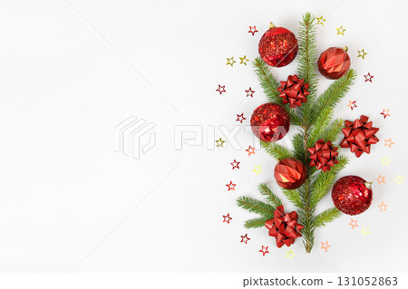 Christmas card made of green Christmas tree branches, red decorative balls, red bows, and glitter stars on gray background with space for text and greetings. Flat lay, copy space 131052863