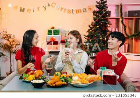 Holiday spirit with Asian friends exchanging gifts, sharing laughs, and enjoying a festive Christmas dinner 131053045