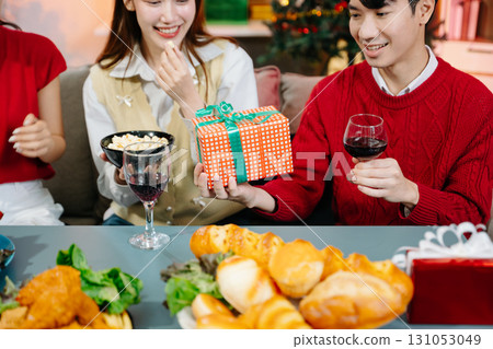 Holiday spirit with Asian friends exchanging gifts, sharing laughs, and enjoying a festive Christmas dinner 131053049
