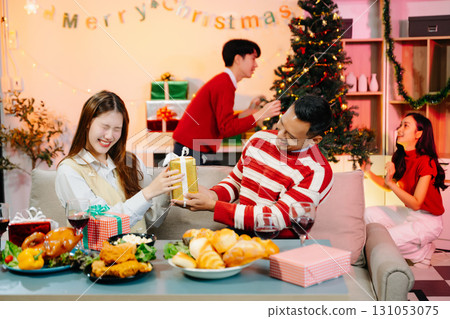 Holiday spirit with Asian friends exchanging gifts, sharing laughs, and enjoying a festive Christmas dinner 131053075