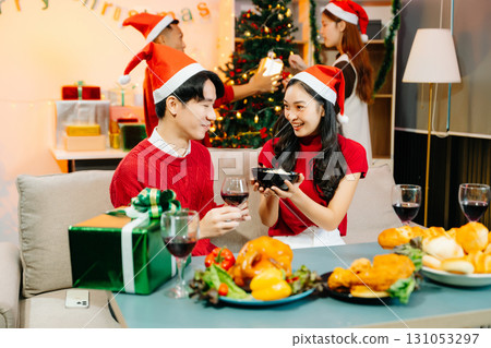 Asian friends capture the holiday spirit with gifts, laughter, and a festive Christmas dinner in a cozy, joy-filled setting 131053297