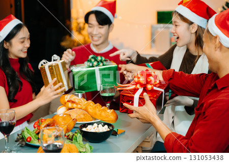 Holiday spirit with Asian friends exchanging gifts, sharing laughs, and enjoying a festive Christmas dinner Holiday spirit with Asian friends exchanging gifts, sharing laughs, and enjoying a festive Christmas dinner 131053438